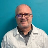 Portrait souriant du fondateur portant une blouse scientifique blanche sur un fond bleu turquoise