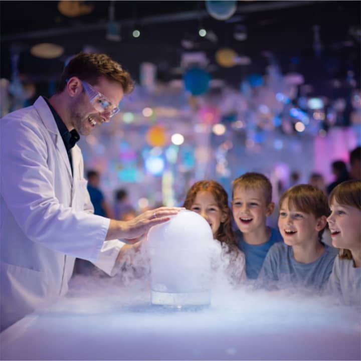 Un animateur scientifique crée un grand nuage de fumée blanche sur une table lumineuse devant quatre enfants émerveillés